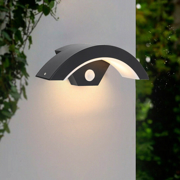 Modern outdoor wall light fixture on a white background with greenery.