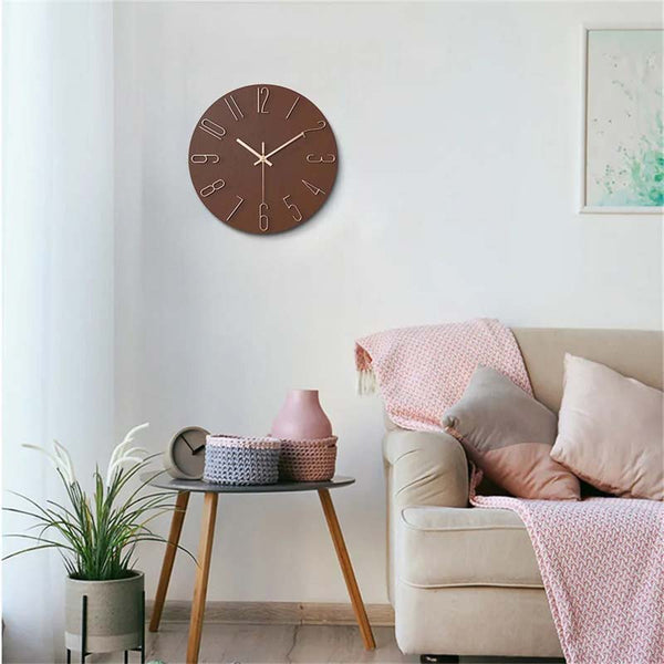 Brown wall clock on a white wall above a beige sofa with pink and gray cushions.
