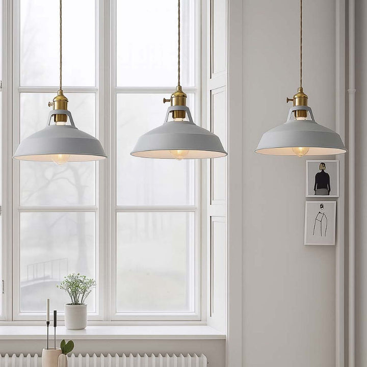 Three gray pendant lights hanging in a room with a window and wall art.