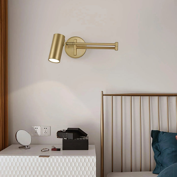 Adjustable Gold wall-mounted lamp on a white dresser with a bed in the background