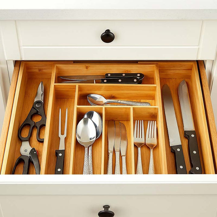 Wooden cutlery organizer with knives, forks, spoons, and scissors inside a drawer.