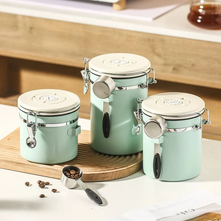 Set of three mint green airtight coffee canisters with cream lids and stainless steel scoops on a wooden board.