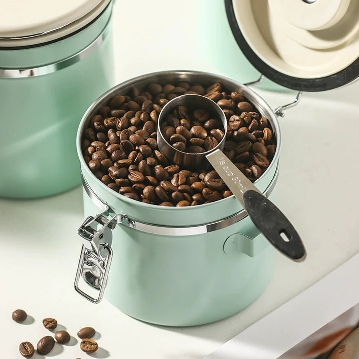 Close-up of mint green coffee canister filled with roasted coffee beans and a scoop resting on top.
