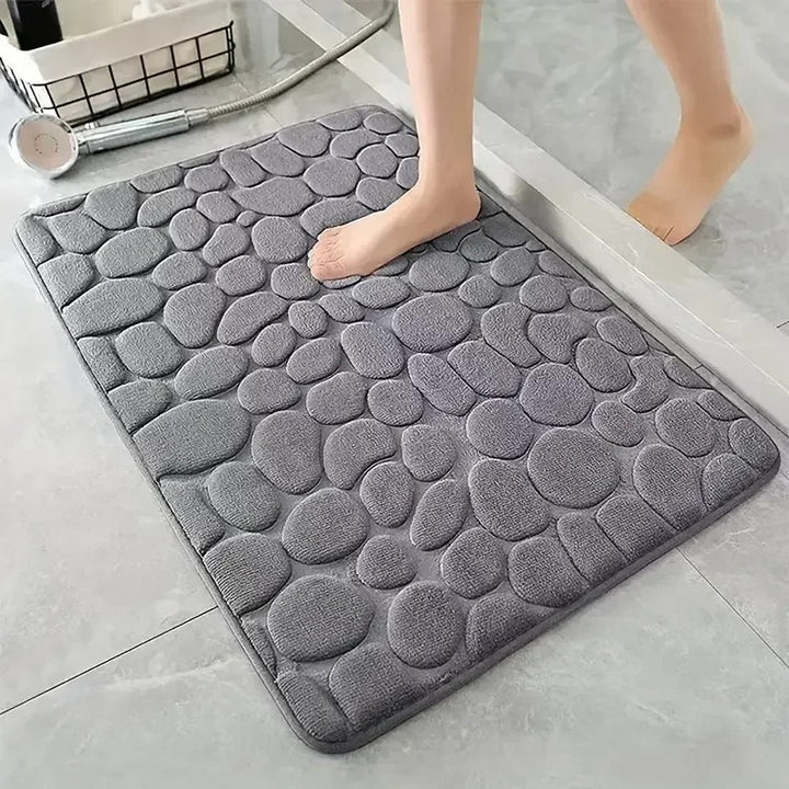 Grey textured bath mat on a bathroom floor with a person stepping onto it.