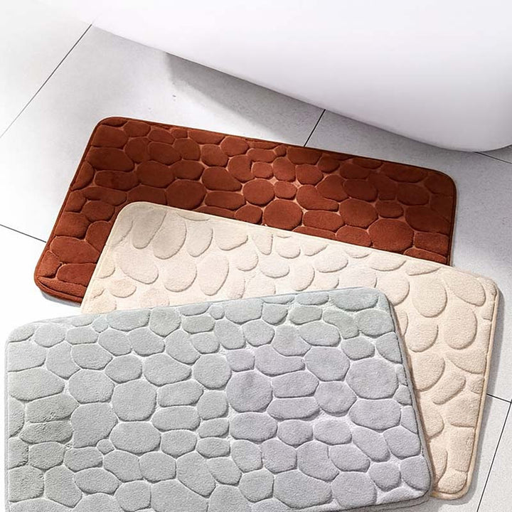 Three textured bath mats in brown, grey, and beige on a tiled floor.