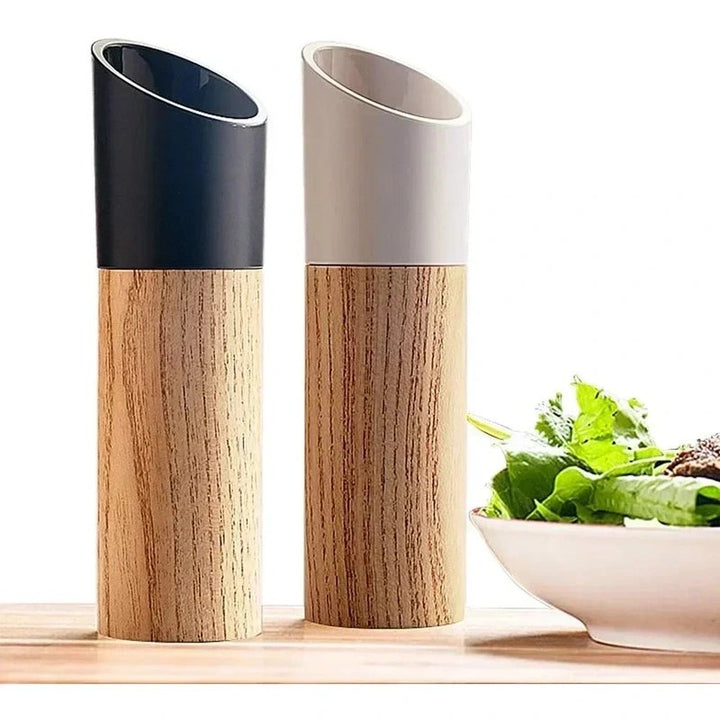 Two wooden salt and pepper grinders on a surface with a bowl of salad in the background.