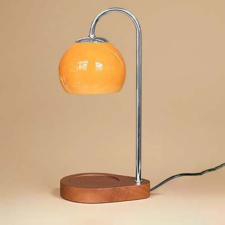 Candle warmer with orange glass shade and wooden base on a beige background