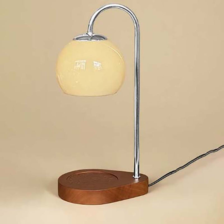 Candle warmer with a yellow glass shade and wooden base on a beige background