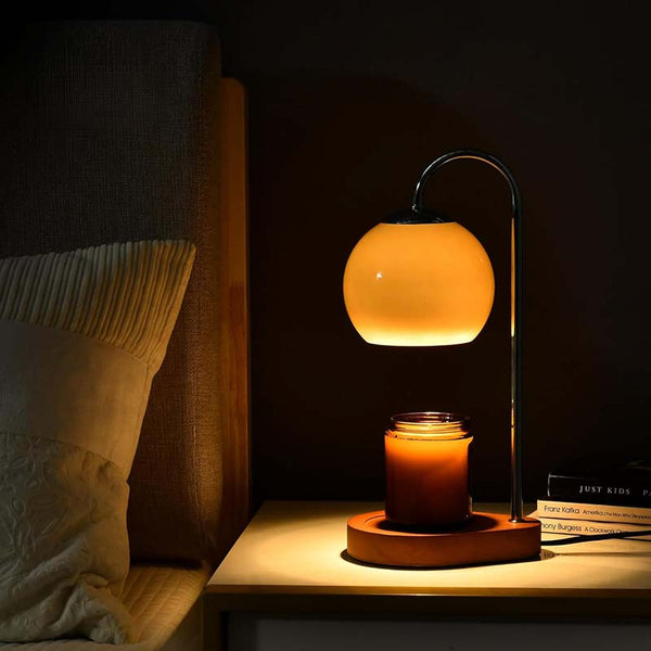 Candle warmer with a glowing yellow light on a bedside table next to books and pillows.
