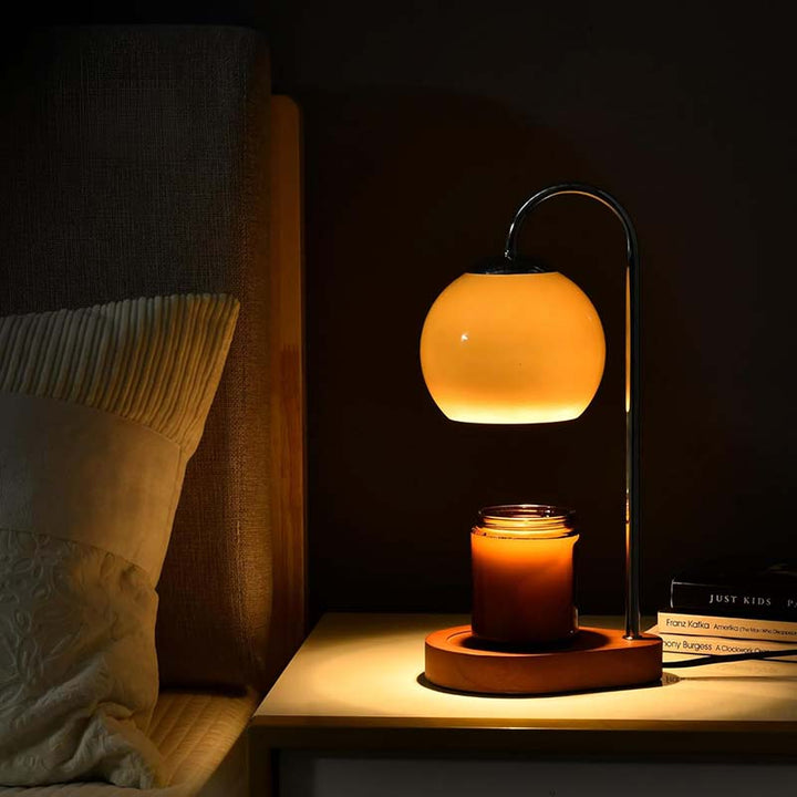 Candle warmer with a glowing yellow light on a bedside table next to books and pillows.
