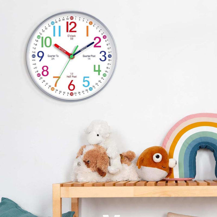 Colorful wall clock on a white wall with toys and a rainbow decoration below.