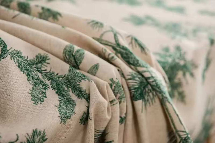 Close-up of Scandinavian cotton linen tablecloth with green pine branch pattern, textured fabric.