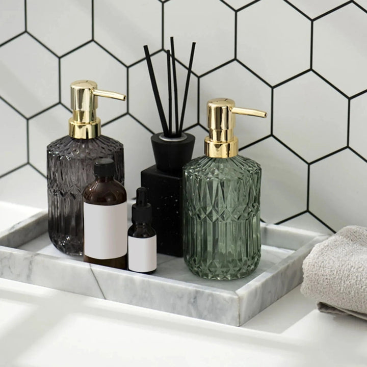 Bathroom counter with glass bottles and a diffuser against a hexagonal tile wall.