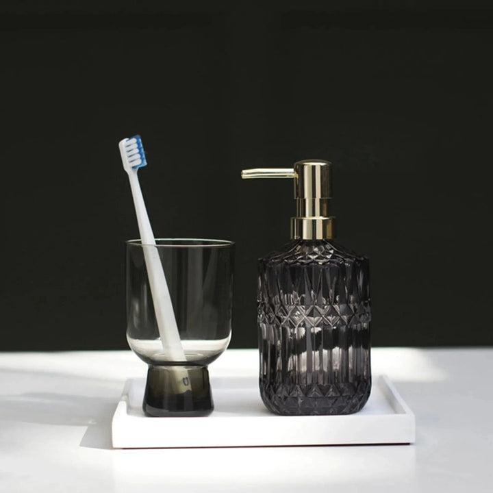 Smoky glass soap dispenser and toothbrush holder on a white surface with a dark background