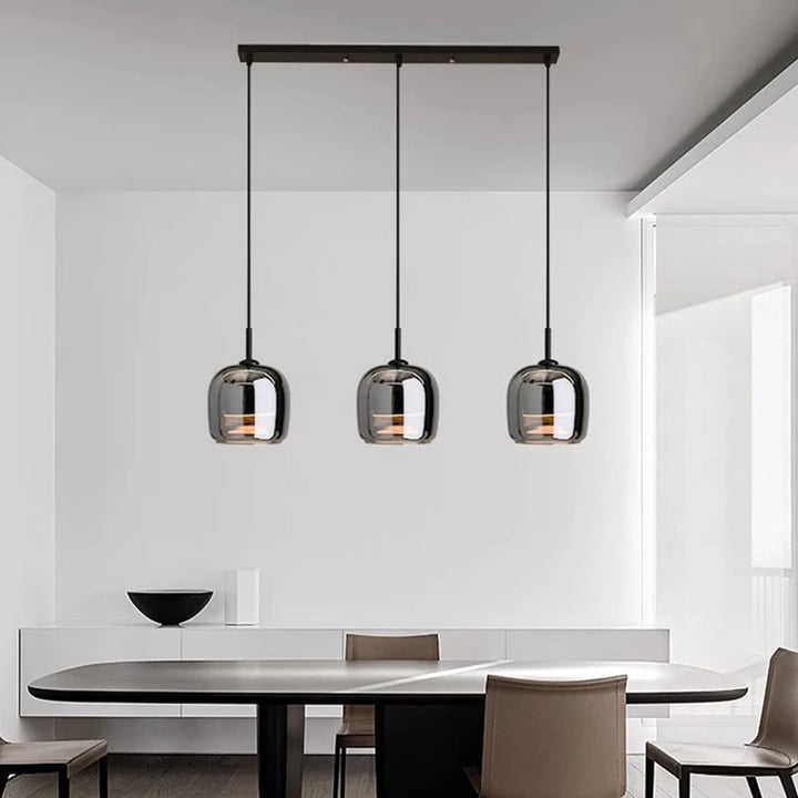 Modern dimmable glass pendant lights hanging above a dining table in a minimalistic room.
