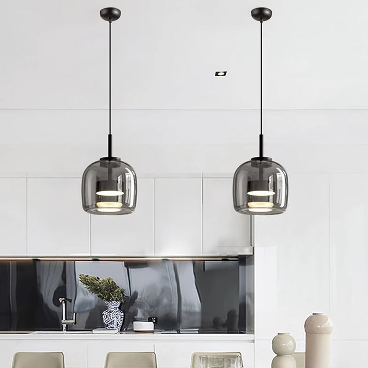 Two nordic glass pendant lights hanging above a kitchen counter with tiled walls.