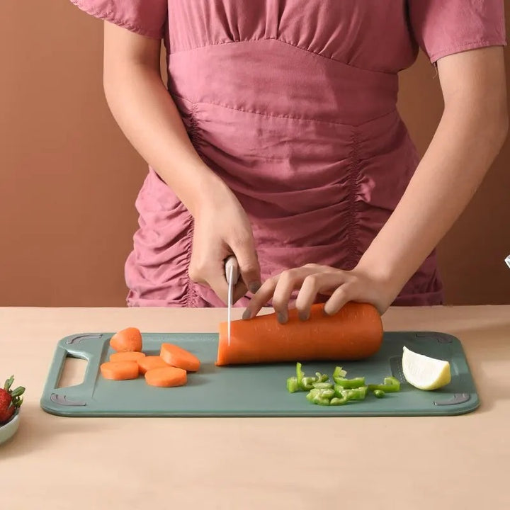Person cutting carrots on a green Stainless-Steel cutting board with a brown background