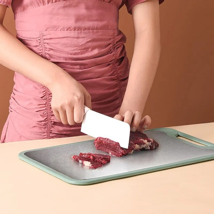 Person cutting meat on a green Stainless-Steel cutting board with a white knife against a brown background