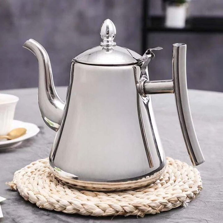 Silver stainless steel induction teapot on a woven trivet with a blurred background