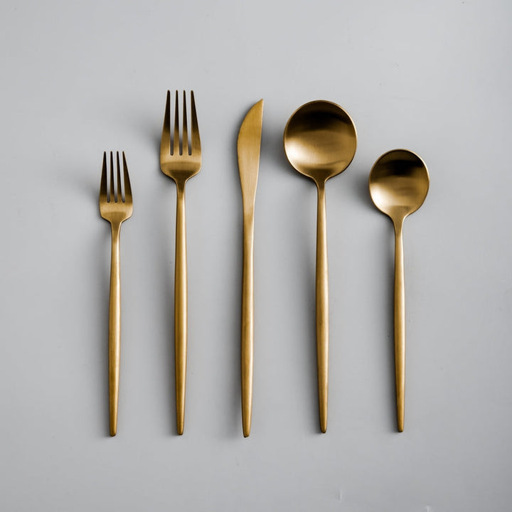 Set of gold cutlery including forks and spoons on a gray background