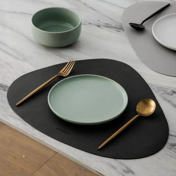 Green ceramic plate with gold fork and spoon on a black placemat, marble background