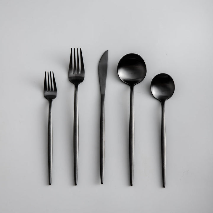 Set of black cutlery including fork, knife, and spoons on a light gray background