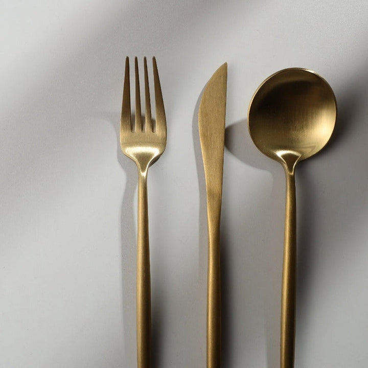 Set of gold fork, knife, and spoon on a light gray background