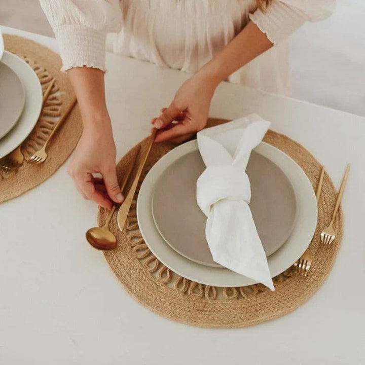 Person setting a table with plates, napkins, and cutlery on a white surface.