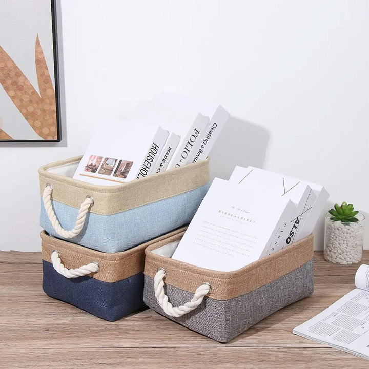Three storage baskets with handles on a wooden surface, containing books and papers.