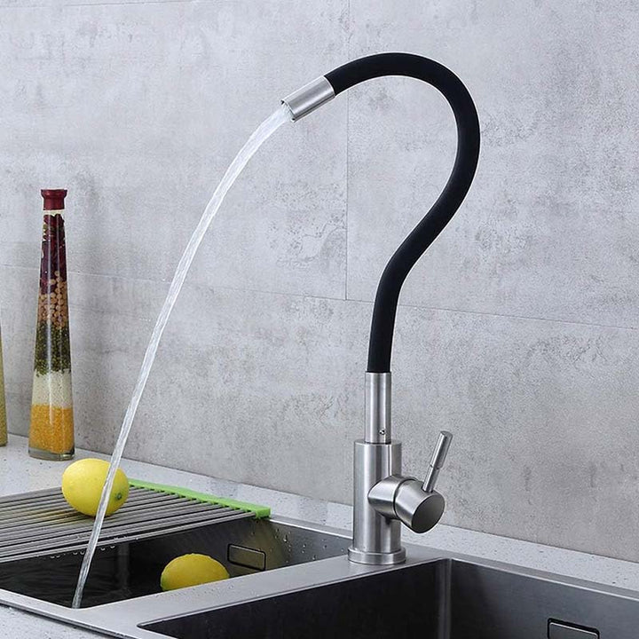 Modern Flexible Kitchen tap with water flowing into a sink against a gray tiled wall.