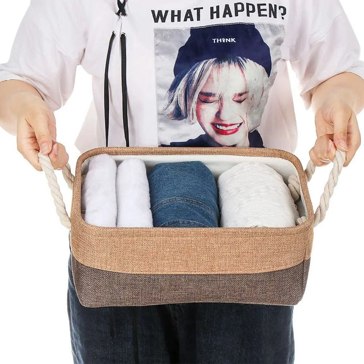 Person holding a brown storage basket with clothes inside, wearing a white shirt with a graphic design.