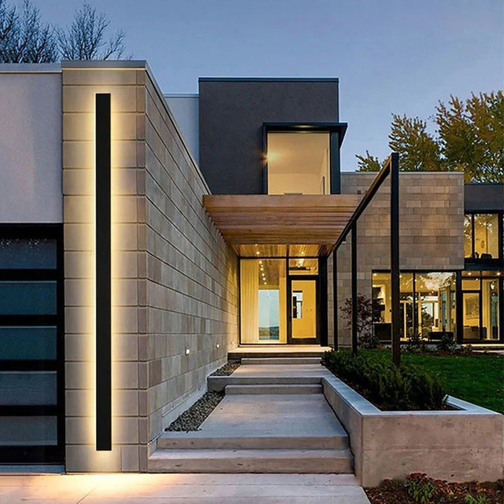 Modern minimalist black LED outdoor wall lamp illuminating entrance of contemporary home exterior