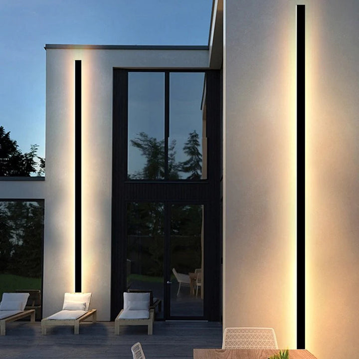 Tall vertical black LED wall lamps glowing warmly on minimalist villa exterior by poolside