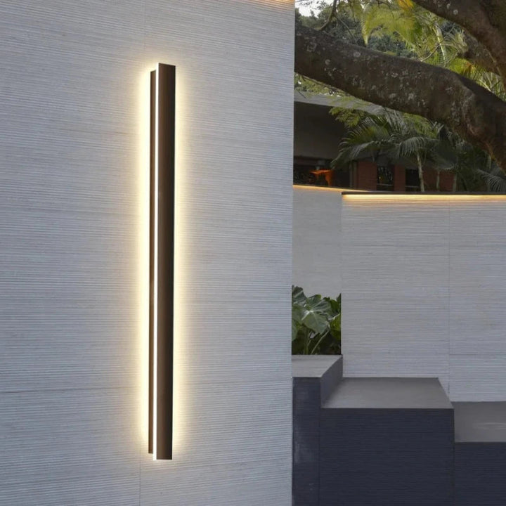 Close-up of slim black LED outdoor wall lamp casting soft light on textured white wall