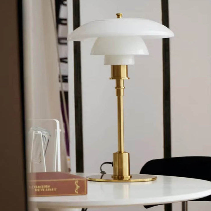 Minimalist Table lamp with white shade and gold base on a table against a blurred background