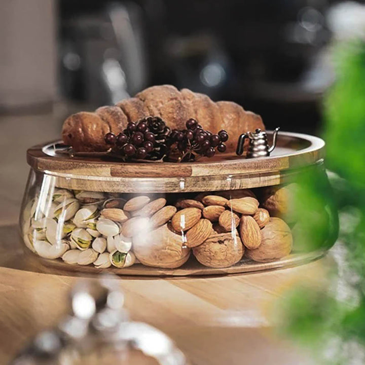 Two-tier glass jar set with acacia lids, neatly storing dried fruit, nuts and olives on a wooden surface.