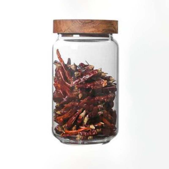 Glass jar with wooden lid containing dried red chili peppers on a white background