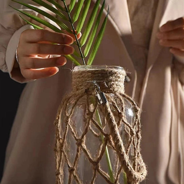 Glass vase with rope netting holding a plant, on a neutral background