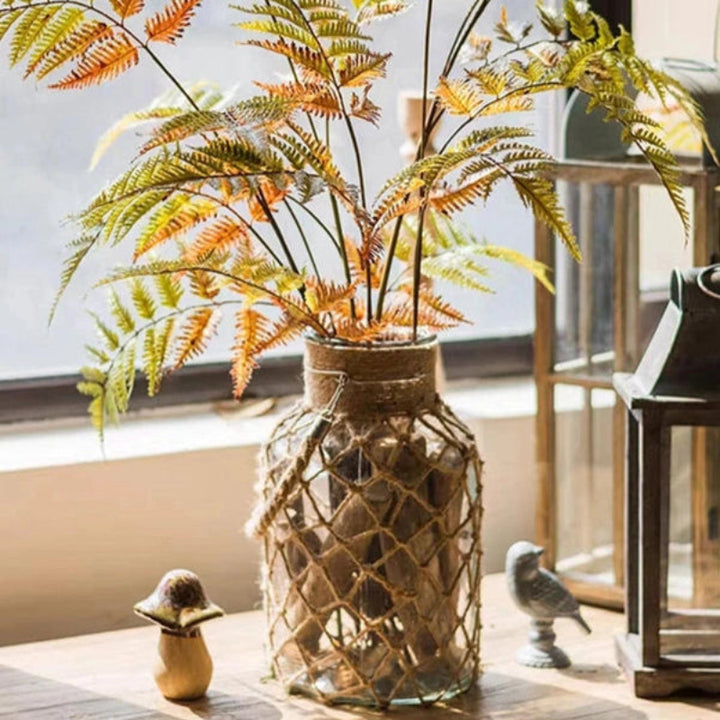 Decorative plant in a glass vase on a windowsill with a view of buildings outside.