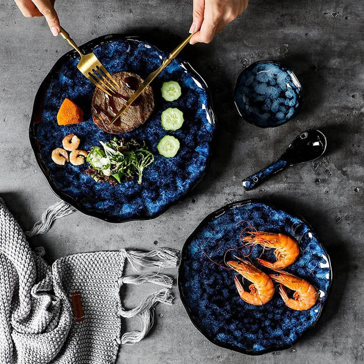Luxury ceramic dinnerware set in navy blue, styled for dining with glossy plates, bowls, and gold cutlery