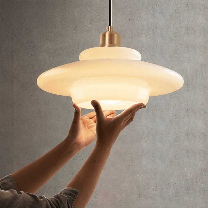 Hands adjusting HAVEN white glass pendant lamp, warm glow with brass holder, Scandinavian lighting design