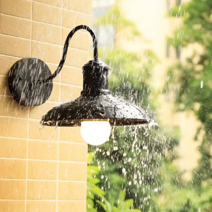 Black retro industrial outdoor wall light illuminated in heavy rain, waterproof LED fixture mounted on tiled exterior wall