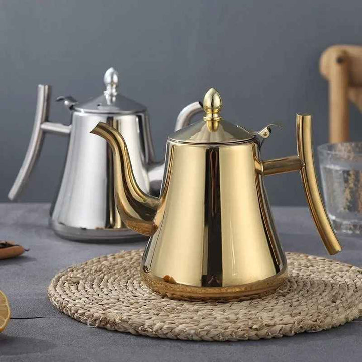 Gold and silver stainless steel induction teapots on a gray surface with a woven mat