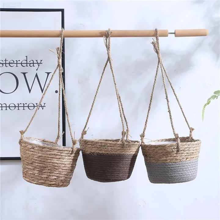 Three woven hanging planters of different colors on a white wall with a framed quote.