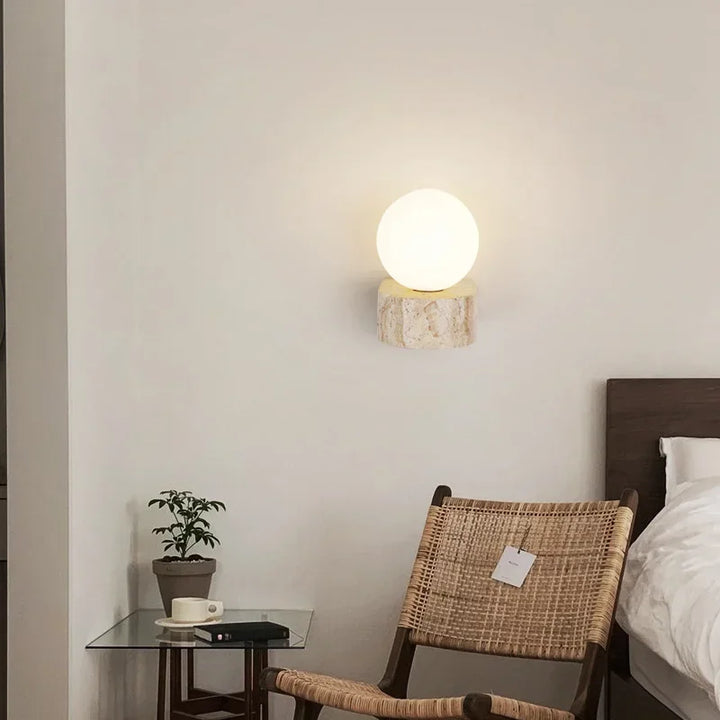 KLOT travertine wall lamp mounted beside bed with woven chair and side table