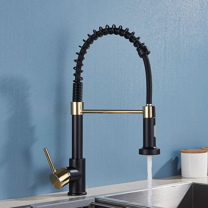 Black and gold kitchen tap with water flowing on a blue wall background