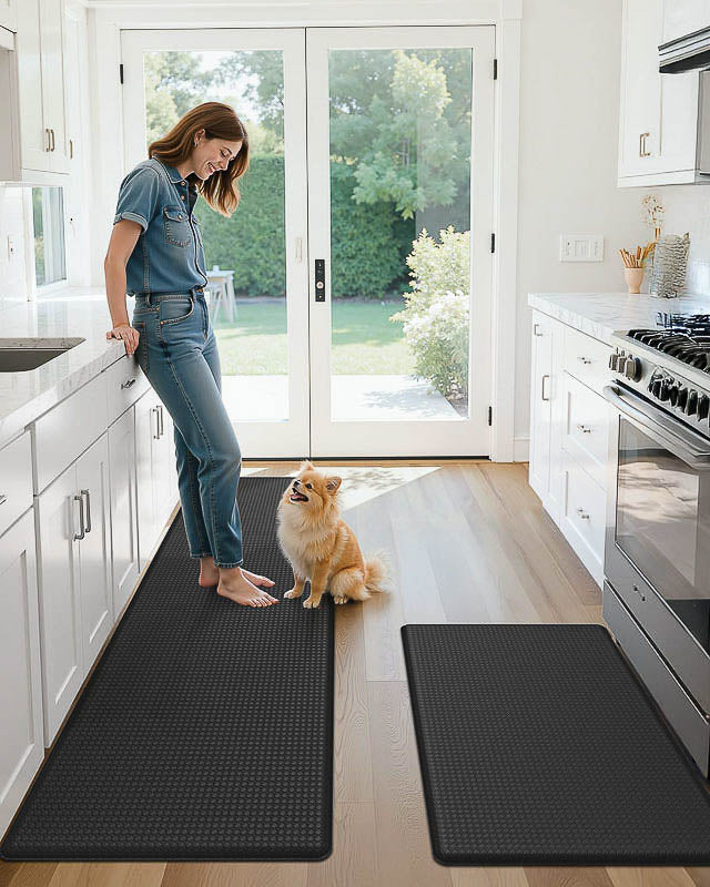 Woman standing in a kitchen with a dog on a black mat, with another mat on the floor.