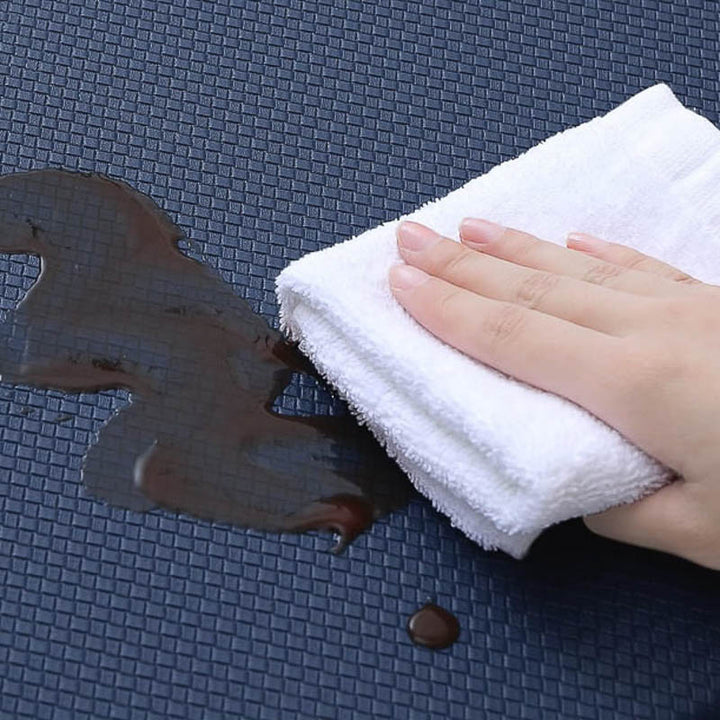 Hand using a white towel to clean up a spill on a dark textured surface