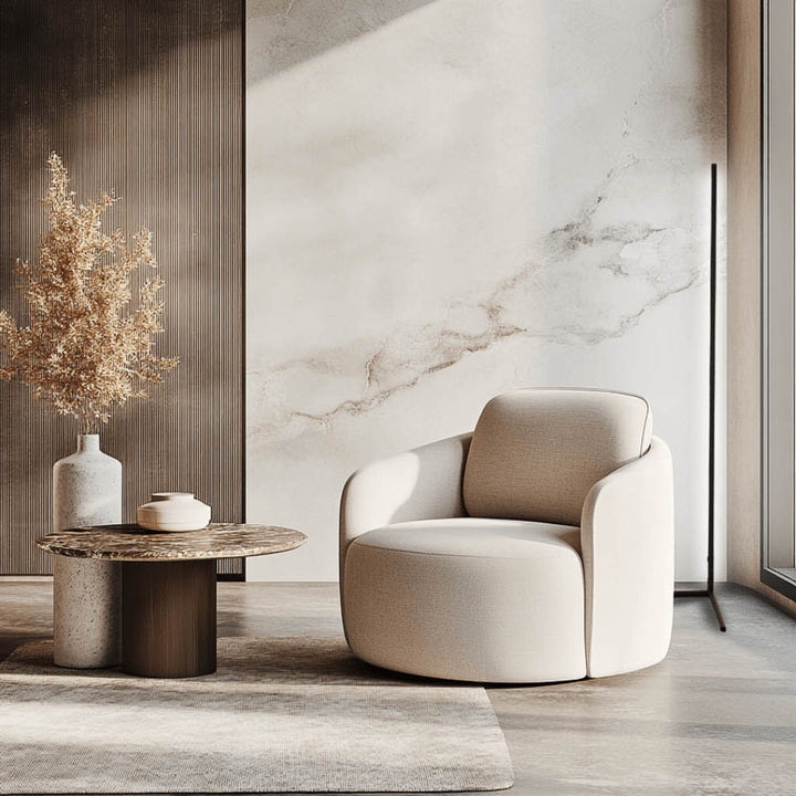 Modern beige armchair and a floor lamp behind it in a stylish room with marble wall and round table.