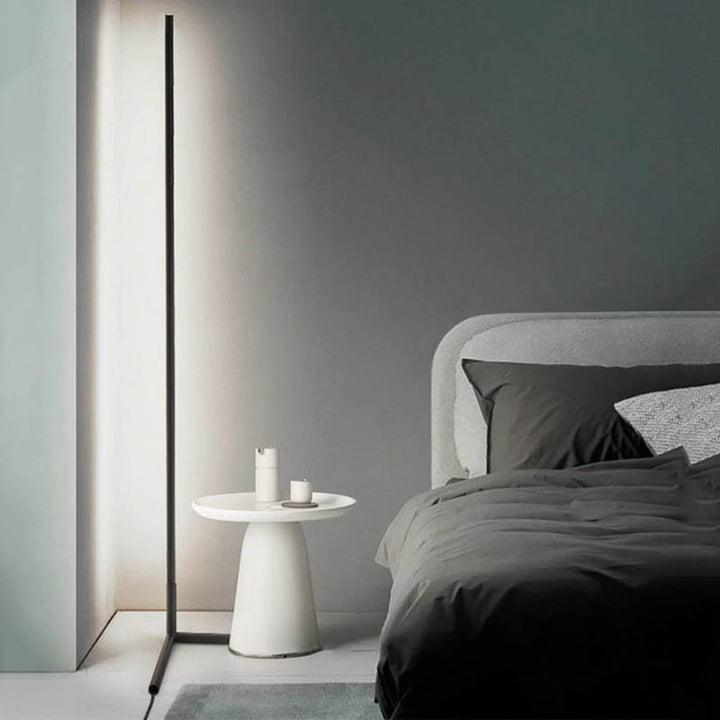 Modern bedroom with a bed, side table, and modern led floor lamp against a gray wall.